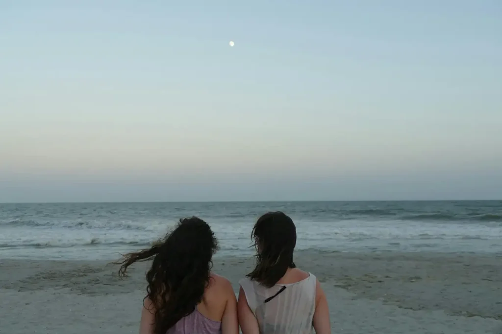 two women sitting on a beach looking at the ocean